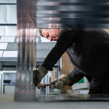 Helta GmbH - Mitarbeiter bearbeitet das Metall mit einem Hammer Helta GmbH - Mitarbeiter bearbeitet das Metall mit einem Hammer